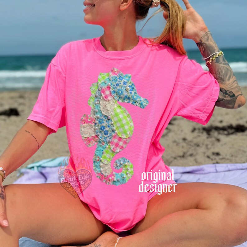 May include: A bright pink t-shirt featuring a colorful seahorse applique. The seahorse design incorporates floral, gingham, and lace fabrics in shades of blue, green, pink, and white. The words "original designer" are printed on the shirt.