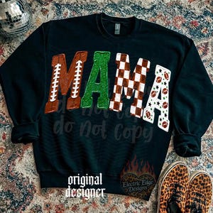 May include: A black long-sleeve sweatshirt featuring the word MAMA in large letters. The M is brown with white football laces, the A is green glitter, the M is a brown and white checkerboard pattern, and the A is white with footballs and stars.