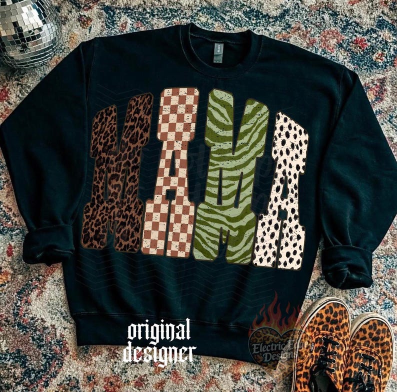 May include: A black long-sleeve sweatshirt featuring the word MAMA in large block letters. Each letter has a distinct pattern: the first M is brown leopard print, the A is a brown and white checkerboard, the second M is green zebra print, and the final A is a white and black dalmatian spot print. The text original designer is printed in white below.