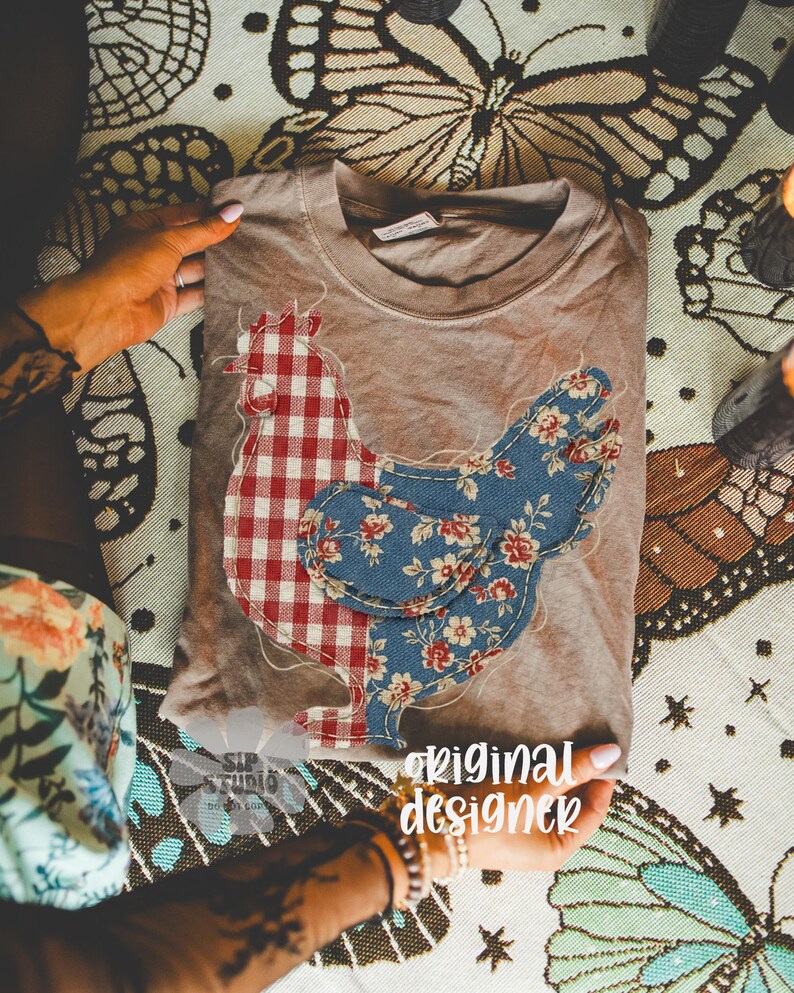 May include: A tan crew neck t-shirt featuring a patchwork chicken design. One side of the chicken is red and white gingham, the other is blue floral. The words "original designer" are visible in the image.