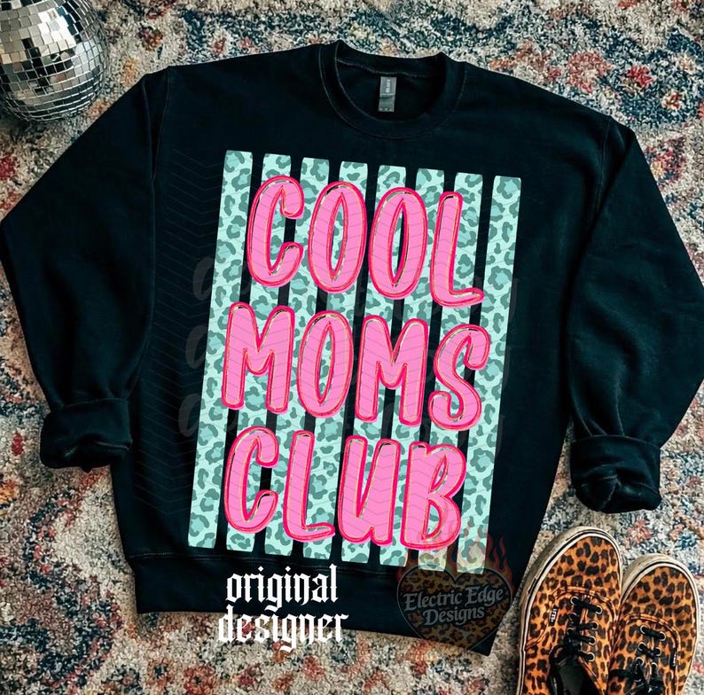 Peut inclure: Sweat-shirt noir avec l'inscription "COOL MOMS CLUB" en rose, soulign&eacute;e d'un rose plus fonc&eacute;. Le texte est plac&eacute; sur un fond bleu clair avec des rayures verticales et un motif l&eacute;opard. Les mots "original designer" sont en bas.
