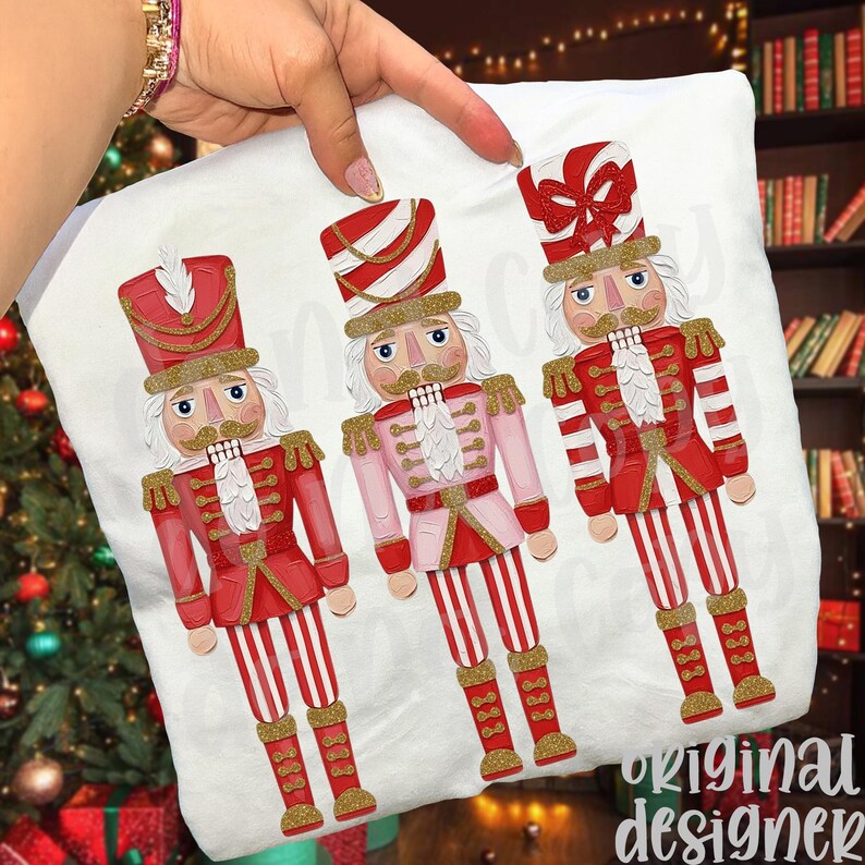 May include: A white pillowcase featuring three decorative nutcracker figures in red and pink uniforms with gold accents. The nutcrackers have white hair and mustaches, and are standing on red and white striped legs. The words "original designer" are printed on the bottom right.