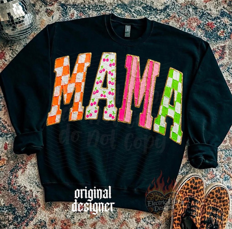 May include: Black sweatshirt with the word "MAMA" in large, colorful letters. The letters have orange checkerboard, cherry print, pink stripes, and green checkerboard patterns. The words "do not copy" and "original designer" are also visible.