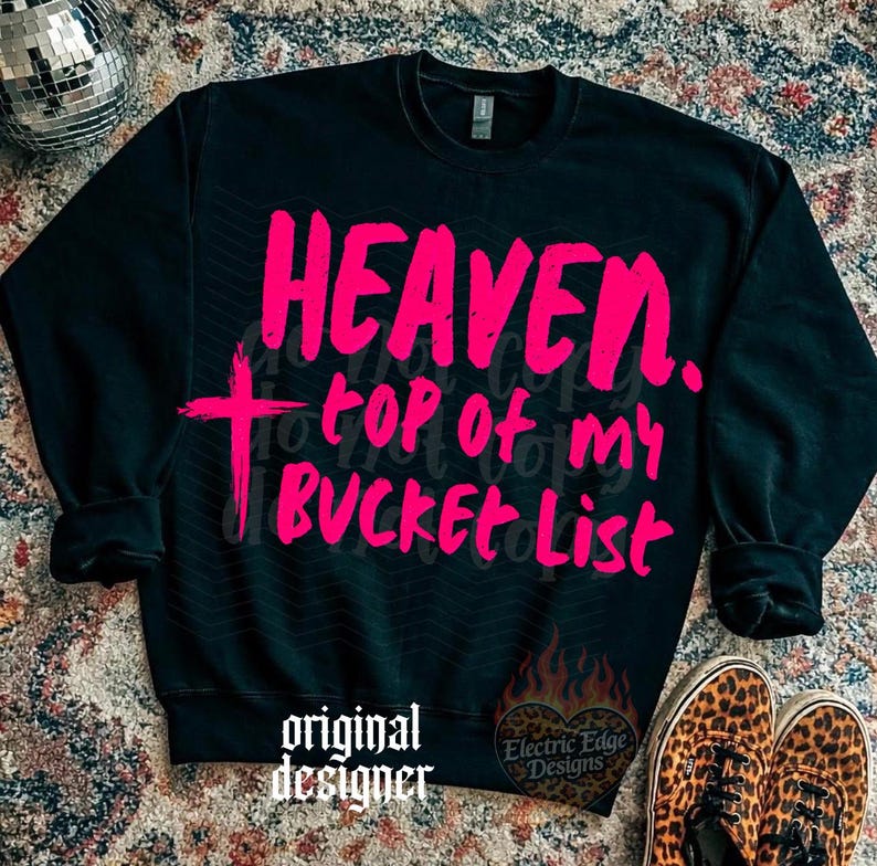 May include: Black sweatshirt with the words "HEAVEN. top of my BUCKET List" in bright pink. A pink cross is on the left side. The words "original designer" are at the bottom left, and a logo is on the bottom right.