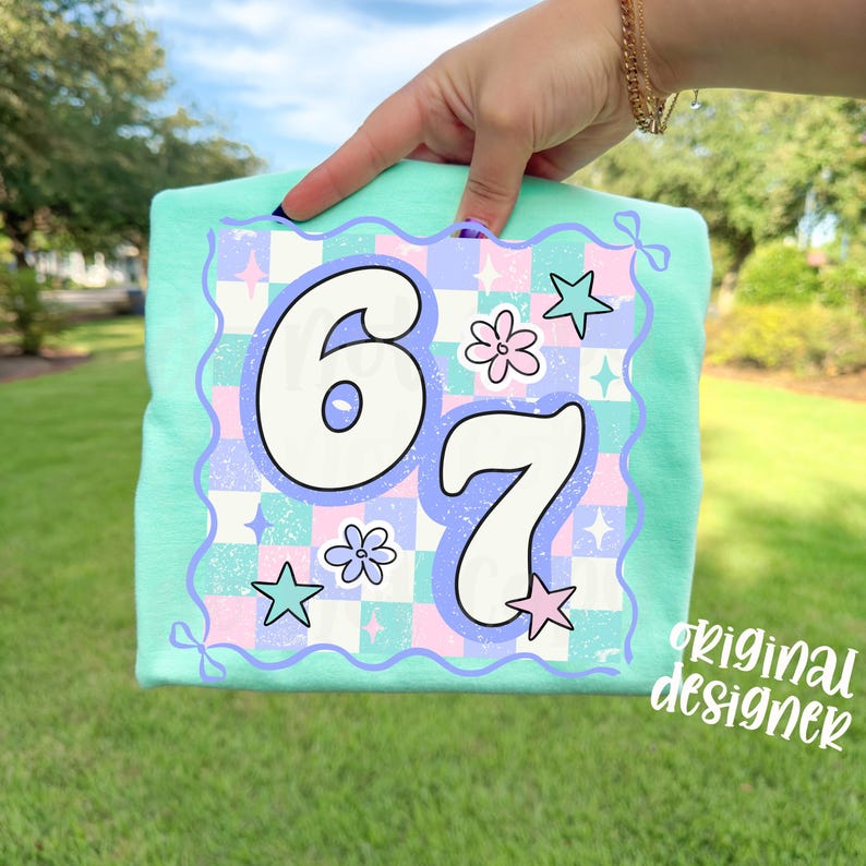 May include: A light green t-shirt with a colorful graphic featuring the numbers "6" and "7" in a retro font. The graphic includes stars, flowers, and a checkered pattern in pastel colors. The text "original designer" is in the bottom right corner.