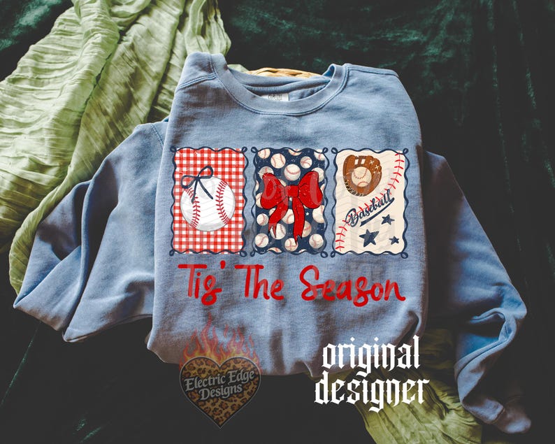 May include: A light blue crewneck sweatshirt featuring a graphic with three rectangular panels. The panels display a baseball with a bow, a red bow over baseballs, and a baseball glove with the text 'Tis The Season' in red script below.