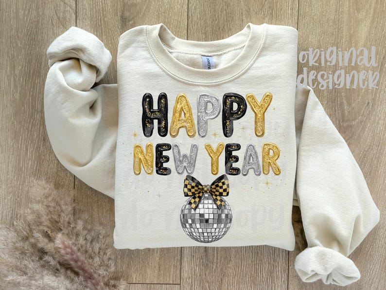 May include: A cream-coloured sweatshirt featuring the text "HAPPY NEW YEAR" in gold, silver, and black bubble letters. A disco ball and bow tie graphic are below the text. The sleeves are rolled up.