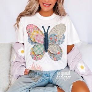May include: White t-shirt featuring a colorful butterfly design. The butterfly is made of various patterned fabrics in pink, blue, and yellow. The shirt also has the text "Electric Edge Designs" and "original designer".