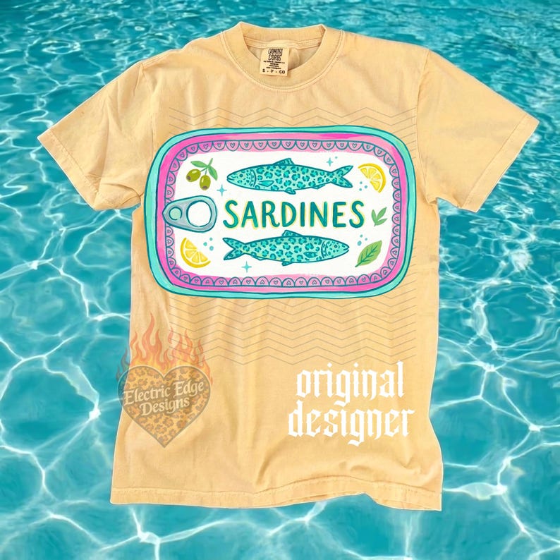 May include: A light yellow t-shirt featuring a sardine can design. The graphic includes two turquoise fish, the word "Sardines", and illustrations of olives and lemon slices. The shirt also has the text "original designer".