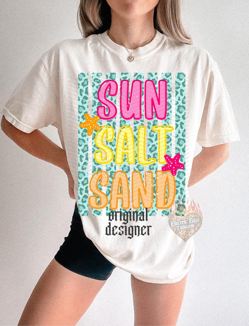 May include: Cream-colored t-shirt with the words "SUN SALT SAND" in pink, yellow, and orange, with starfish accents. The design is set against a teal leopard print background. The words "original designer" are below the main text.