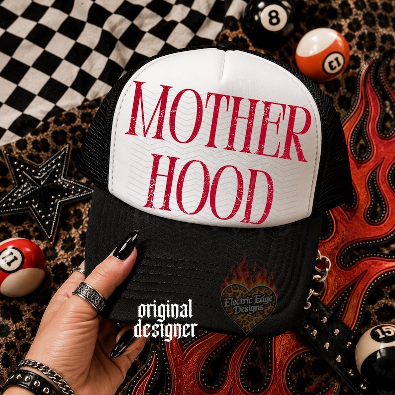 May include: A black and white trucker hat featuring the text MOTHER HOOD in distressed red lettering on the front panel. The hat has a white foam front, a black mesh back, and a black brim. A small logo with the text Electric Edge Designs is visible.