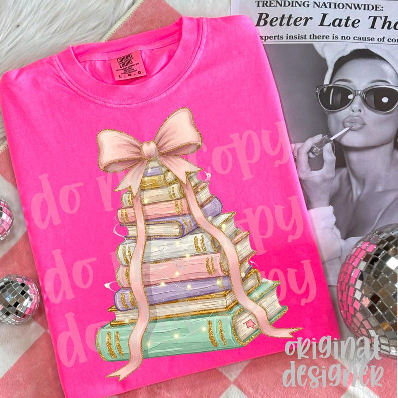 May include: Bright pink sweatshirt featuring a stack of books with a pink bow and ribbon. The books have gold accents and are in pastel colors. The text "do copy" is printed on the shirt.