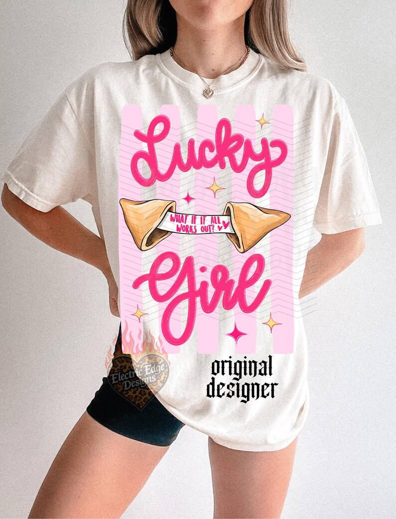May include: Off-white t-shirt featuring a pink graphic with the words "Lucky Girl." The design includes a fortune cookie with the text "What if it all works out?" and star accents. The words "original designer" are also printed on the shirt.