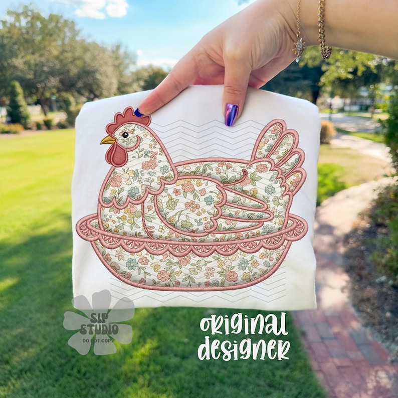 May include: White t-shirt featuring an embroidered hen design. The hen is in a nest, with floral patterns in pink, yellow, and blue. The design includes the text "original designer" and "SIP STUDIO DO NOT COPY".