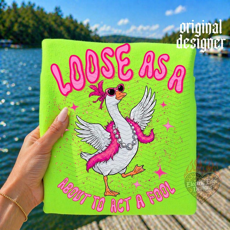 May include: A neon green t-shirt with the phrase "LOOSE AS A ABOUT TO ACT A FOOL" in pink, featuring a cartoon goose wearing sunglasses, a pink boa, and a pearl necklace. The design includes pink stars and the words "original designer" and "Electric Edge Designs".