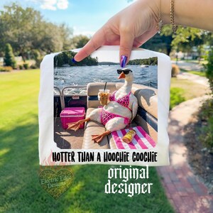 Puede incluir: Camiseta blanca con un ganso con gafas de sol y un bikini rosa con estampado de leopardo, sosteniendo una bebida en un barco. El texto dice "HOTTER THAN A HOOCHIE COOCHIE" y "original designer".