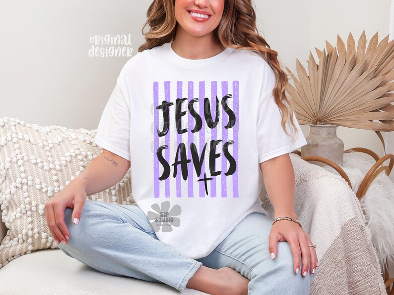 May include: White t-shirt with the text "JESUS SAVES" in black, set against a vertical striped background of purple and white. The shirt has a crew neck and short sleeves. The design includes a cross symbol.