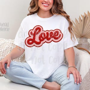 May include: White t-shirt with a red glitter "Love" design. The word "Love" is in a bold, rounded font with a pink outline. The shirt is a casual style, suitable for everyday wear.