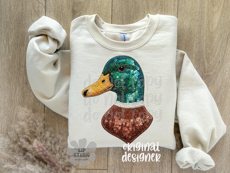 Pu&ograve; includere: Felpa color crema con un design dettagliato di un'anatra. La testa dell'anatra &egrave; adornata da paillettes verdi, un becco giallo perlato e un petto con paillettes marroni. Le maniche sono arrotolate e le parole "original designer" sono stampate in basso a destra.