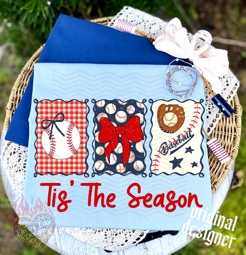 May include: A light blue t-shirt featuring three rectangular panels with baseball-themed graphics, including a baseball with a bow, a red bow, and a baseball glove. The text 'Tis The Season' is printed in red below the panels in a script font.