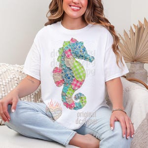 May include: White t-shirt featuring a colorful seahorse design made of patchwork fabric. The seahorse has blue floral, pink gingham, and green plaid patterns. The shirt also has the text "original designer".