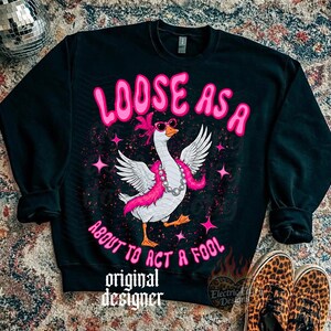 May include: Black sweatshirt featuring a goose graphic with sunglasses, a pink boa, and a pearl necklace. The text "LOOSE AS A ABOUT TO ACT A FOOL" is above and below the goose. The words "original designer" are at the bottom.