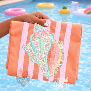 May include: An orange beach towel with pink chevron stripes and a large seashell illustration. The seashell is detailed with various colors and sea life imagery. The towel is held near a pool with inflatable toys.