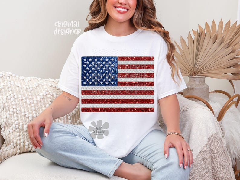 May include: White t-shirt featuring a glittery American flag design. The flag has a blue square with white stars and red and white stripes. The shirt has short sleeves and a crew neck. The words "original designer" are printed on the top left.