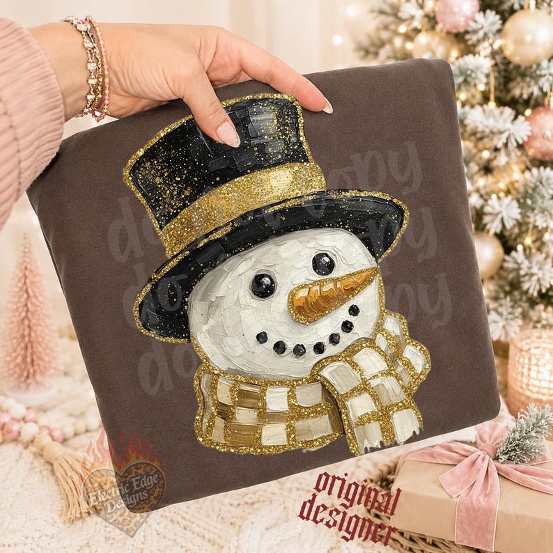 May include: A dark brown sweatshirt featuring a graphic of a snowman wearing a black top hat with a gold glitter band, a gold glitter carrot nose, and a gold and white checkered scarf. The design has a textured, painted appearance.