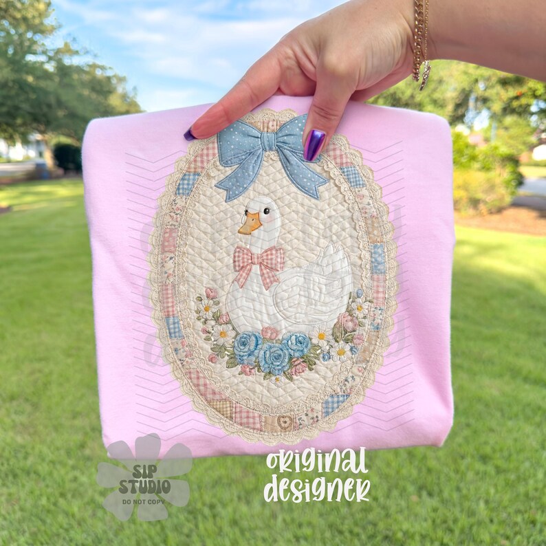 May include: Pink t-shirt featuring an embroidered oval design with a white goose wearing a pink bow tie, surrounded by flowers and a blue bow. The text "original designer" is visible.