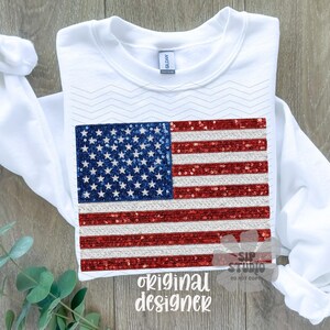 May include: White long-sleeve sweatshirt featuring a sequined American flag design. The flag has a blue square with white stars and red and silver stripes. The words "original designer" are printed at the bottom.