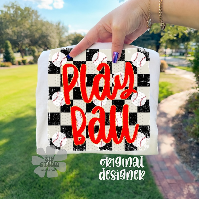 May include: White t-shirt with a baseball-themed design. The design features a checkerboard pattern with baseballs and the words "Play Ball" in red. The shirt also has the text "original designer".