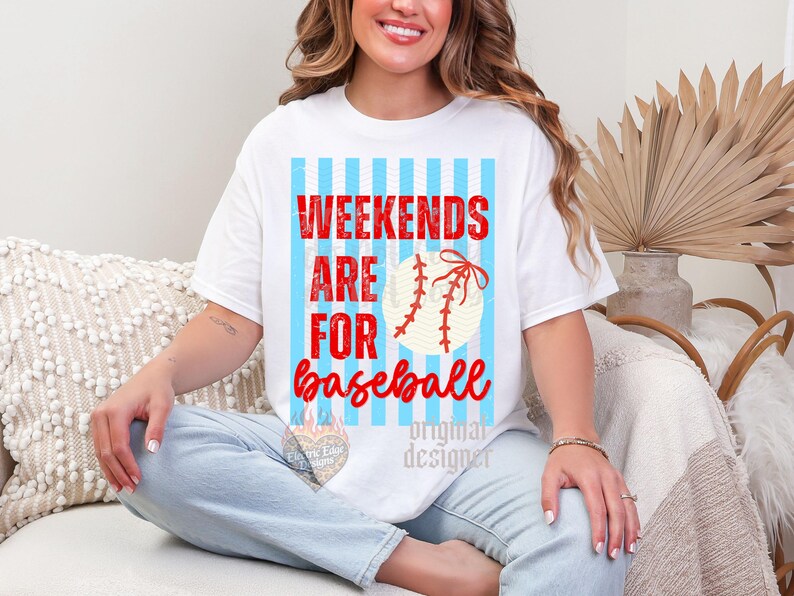 May include: White t-shirt with the text "Weekends are for baseball" in red and a baseball graphic. The design features a light blue striped background. The shirt is a casual, everyday wear item.