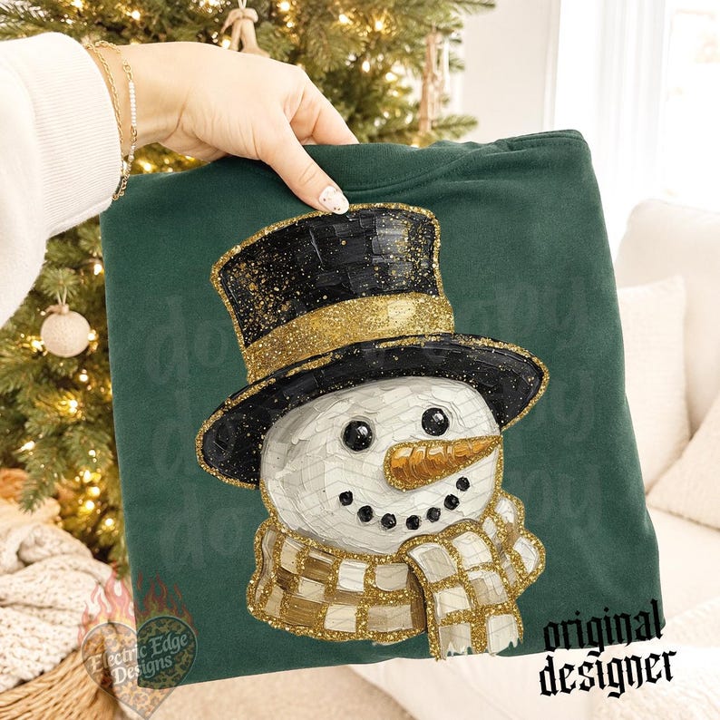 May include: A dark green sweatshirt featuring a graphic of a snowman wearing a black top hat with gold glitter accents. The snowman has a textured white face, a gold glittery carrot nose, and a gold and white checkered scarf with glitter details.