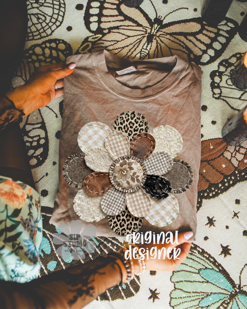 May include: A brown t-shirt with a large, appliqued flower design. The flower petals feature various textures and patterns, including leopard print, gingham, and lace. The text "original designer" is visible.