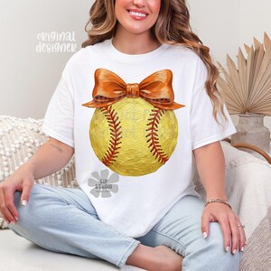Pu&ograve; includere: T-shirt bianco con un design di softball giallo, cuciture rosse e un grande fiocco arancione. Il testo "original designer" &egrave; visibile in alto a sinistra e "SIP STUDIO" in basso. Un design casual e sportivo.