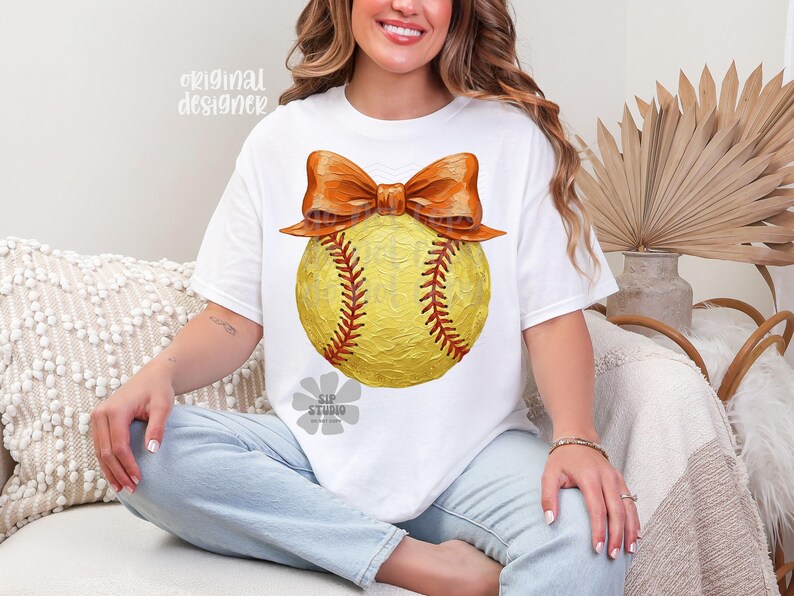 Pu&ograve; includere: T-shirt bianco con un design di softball giallo, cuciture rosse e un grande fiocco arancione. Il testo "original designer" &egrave; visibile in alto a sinistra e "SIP STUDIO" in basso. Un design casual e sportivo.