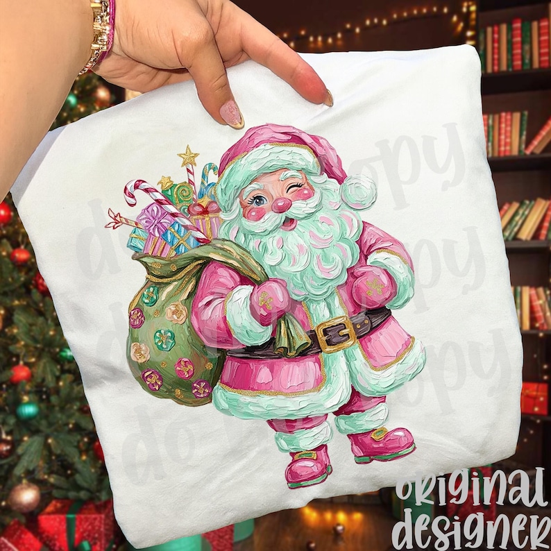 May include: A white cushion with a festive illustration of Santa Claus in pink and mint green attire, carrying a sack of gifts. The design includes candy canes, wrapped presents, and a gold star. The cushion is held by a hand.