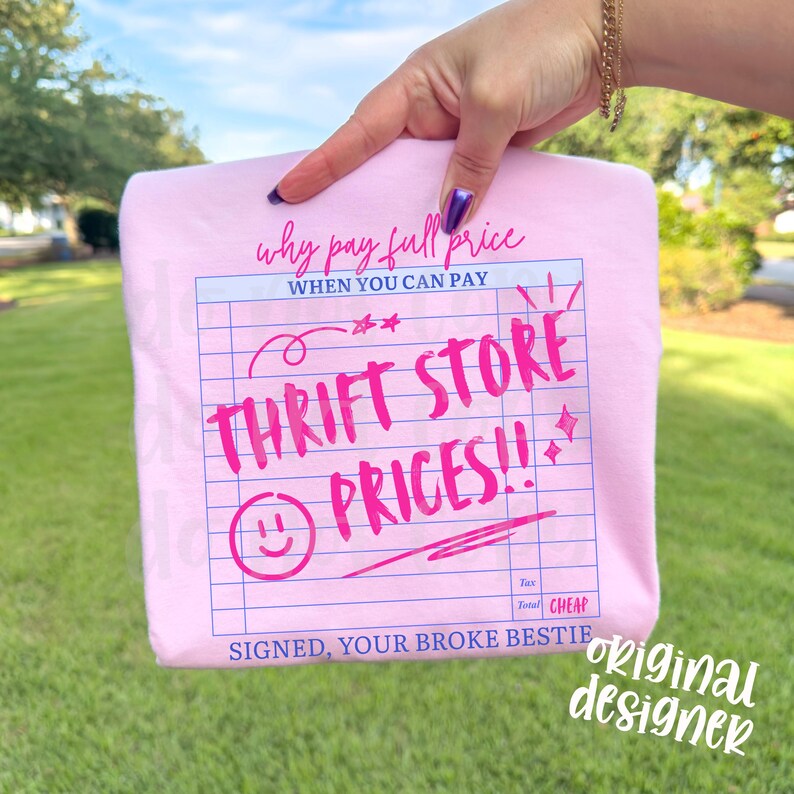 May include: A light pink t-shirt with the text "Why pay full price when you can pay Thrift Store Prices!!" in a handwritten style. The design resembles a receipt with a smiley face and stars. The words "Signed, Your Broke Bestie" are also included.
