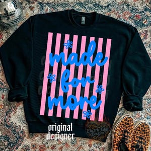 May include: Black sweatshirt with the text "made for more" in blue script over pink vertical stripes. The design includes small blue flower accents. The words "original designer" are at the bottom.