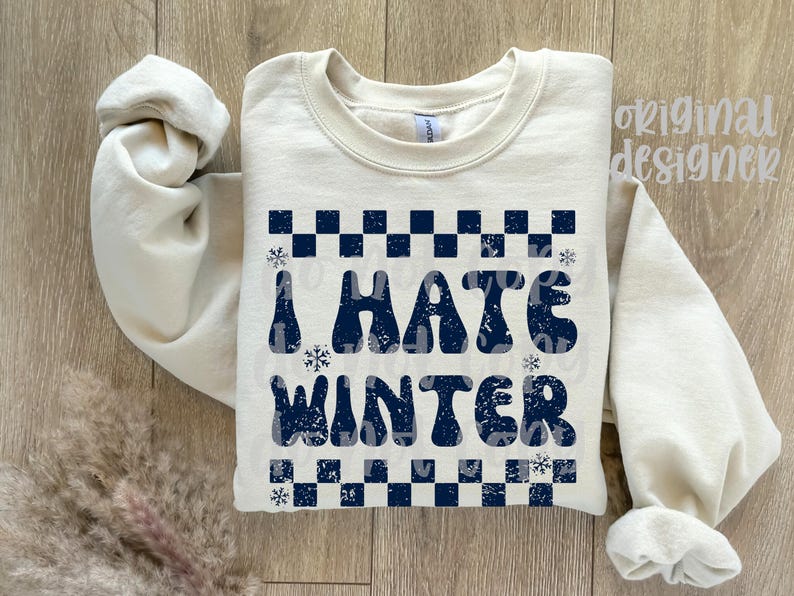 May include: Cream-colored sweatshirt with the phrase "I HATE WINTER" in navy blue, featuring a checkered pattern and snowflakes. The sweatshirt has long sleeves and a crew neck.