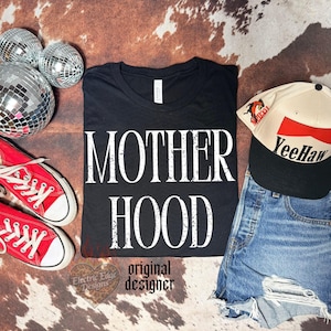 May include: A black t-shirt with the white distressed text MOTHER HOOD, paired with red canvas sneakers, a cream and black baseball cap with the text YeeHaw, and three silver disco balls. The shirt features a white neck label.