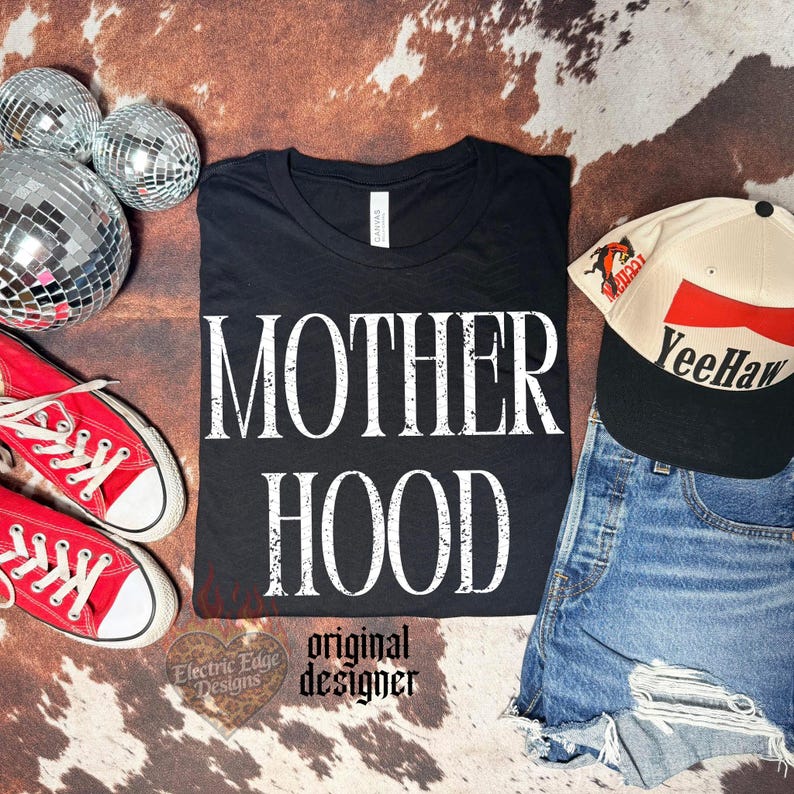 May include: A black t-shirt with the white distressed text MOTHER HOOD, paired with red canvas sneakers, a cream and black baseball cap with the text YeeHaw, and three silver disco balls. The shirt features a white neck label.