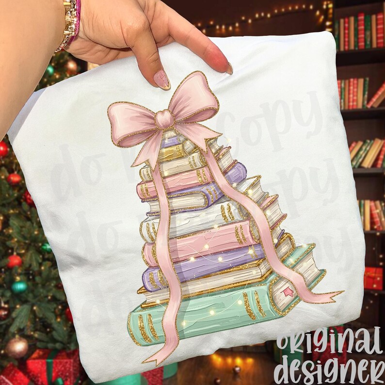 May include: White pillow with a design of a stack of books in pastel colors, topped with a pink bow and ribbon. The books have gold accents and are decorated with string lights. The words "original designer" are in the bottom right corner.