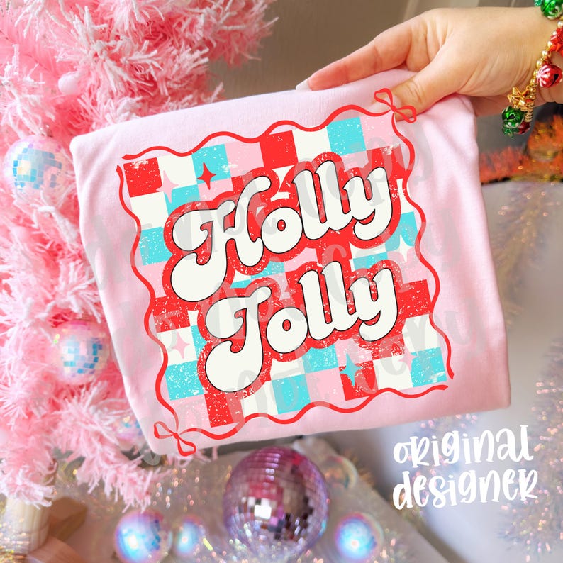 May include: A light pink t-shirt with the words "Holly Jolly" in a retro font. The design features a red and blue checkered pattern with stars. The words are outlined in red and white. The words "original designer" are in the bottom right corner.