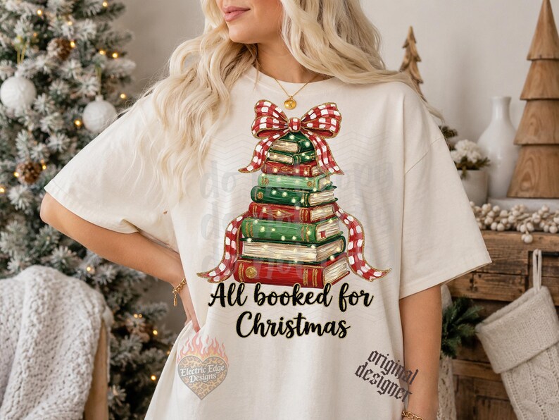 May include: An off-white short-sleeve t-shirt featuring a graphic of a Christmas tree made of stacked books topped with a red and white plaid bow. The text All booked for Christmas is printed in black below the book stack illustration.