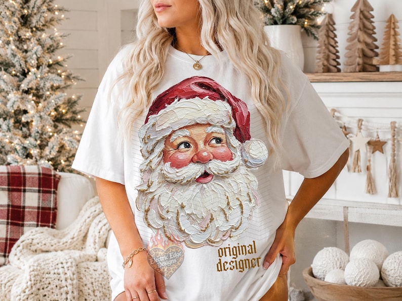 Puede incluir: Una camiseta blanca de manga corta con un gr&aacute;fico texturizado de estilo empaste que muestra a Santa Claus con un gorro rojo. El dise&ntilde;o incluye una barba y un bigote blancos y gruesos con pinceladas visibles. El texto "original designer" est&aacute; impreso en dorado.