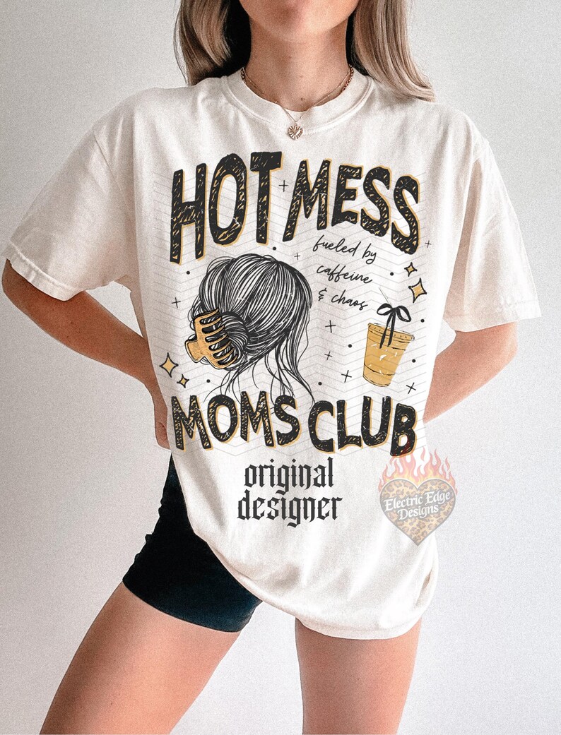 May include: Cream-colored t-shirt with the text "HOT MESS MOMS CLUB" in black and yellow. The shirt features a graphic of a woman's hair, a coffee cup, and the words "fueled by caffeine & chaos".
