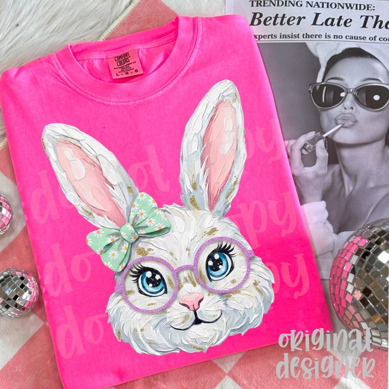 May include: A bright pink Comfort Colors sweatshirt featuring a detailed illustration of a white bunny wearing glasses and a bow. The bunny has blue eyes and gold accents. The words "do" and "happy" are printed on the shirt.