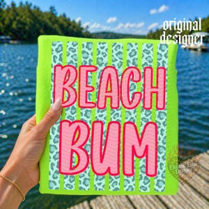 May include: A neon green beach towel with the words "BEACH BUM" in pink, outlined in red. The towel has a leopard print design in light blue and green stripes. The words "original designer" are printed in white.